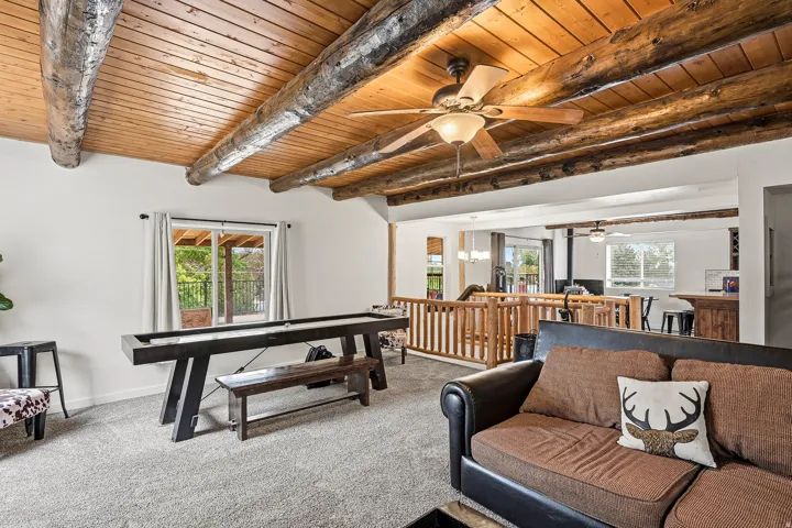 Vaulted wood plank ceiling with exposed log beams and a ceiling fan, light gray carpet flooring, and a sliding glass door