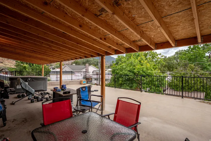 Covered outdoor patio with exposed wood joists, concrete flooring, and black metal railing