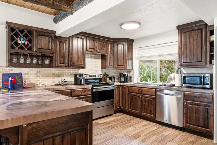 Dark wood cabinetry, stainless steel appliances, wood-finish flooring, mosaic tile backsplash, and a built-in wine rack with stemware storage