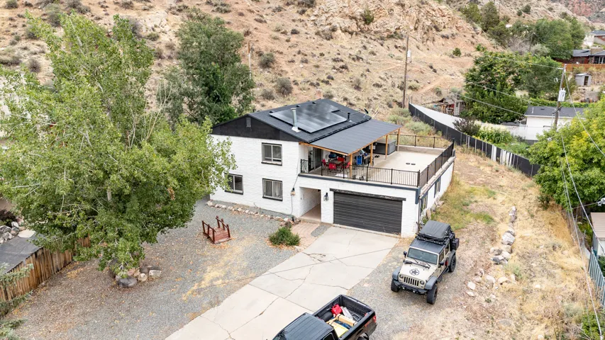 White exterior with black trim, rooftop solar panels, an attached garage, and an upper-level deck with black railing