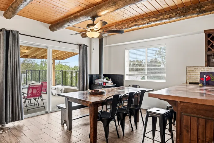 Wood-plank ceiling with exposed beams, wood-finish flooring, built-in bar with wood-paneled base, and sliding glass doors to outdoor patio