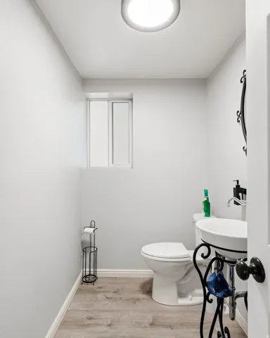 Recessed lighting illuminates the space, featuring a window, wood-finish flooring, and a pedestal sink