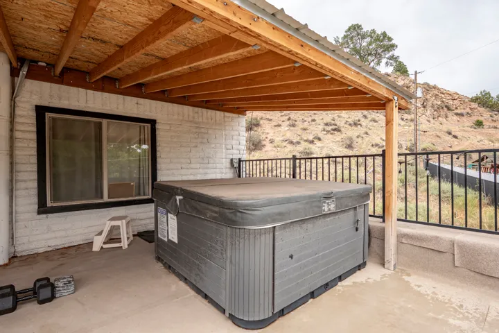 Covered patio with a spa, white painted brick exterior, and a black metal railing
