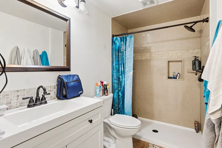 White vanity with dark hardware, framed mirror, and a mosaic tile backsplash