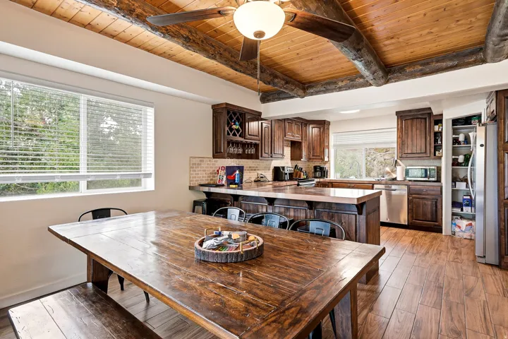 Wood-finish flooring, exposed wood beam ceiling, wood cabinetry, large window with blinds, and a built-in wine rack
