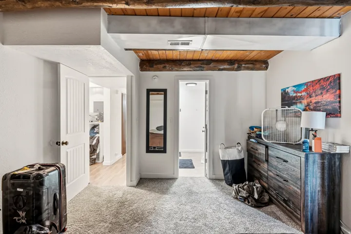 Exposed wood beam ceiling with a visible duct, light gray carpeting, and white paneled interior doors