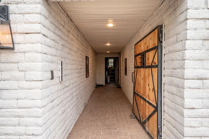 White-painted brick walls, brick paver flooring, recessed ceiling lighting, and a wood-panel door with metal accents