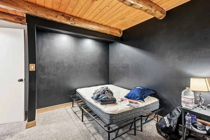 Recessed lighting illuminates the dark-painted wall, complemented by a wood-paneled ceiling with exposed log beams