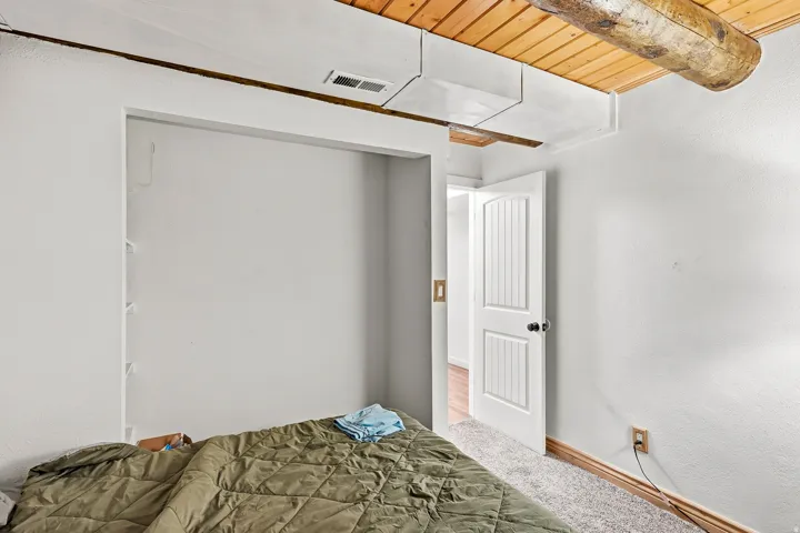 Wood-paneled ceiling with exposed wood beams, white paneled interior door, and light-colored carpeting