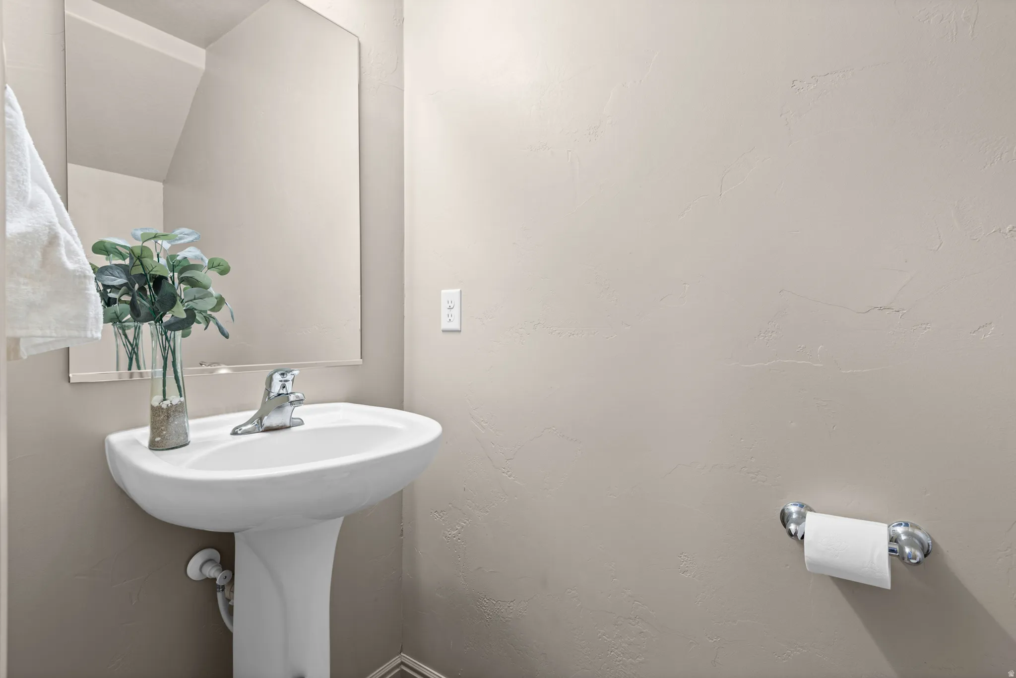 Pedestal sink with a chrome faucet, large wall mirror, and textured wall finish