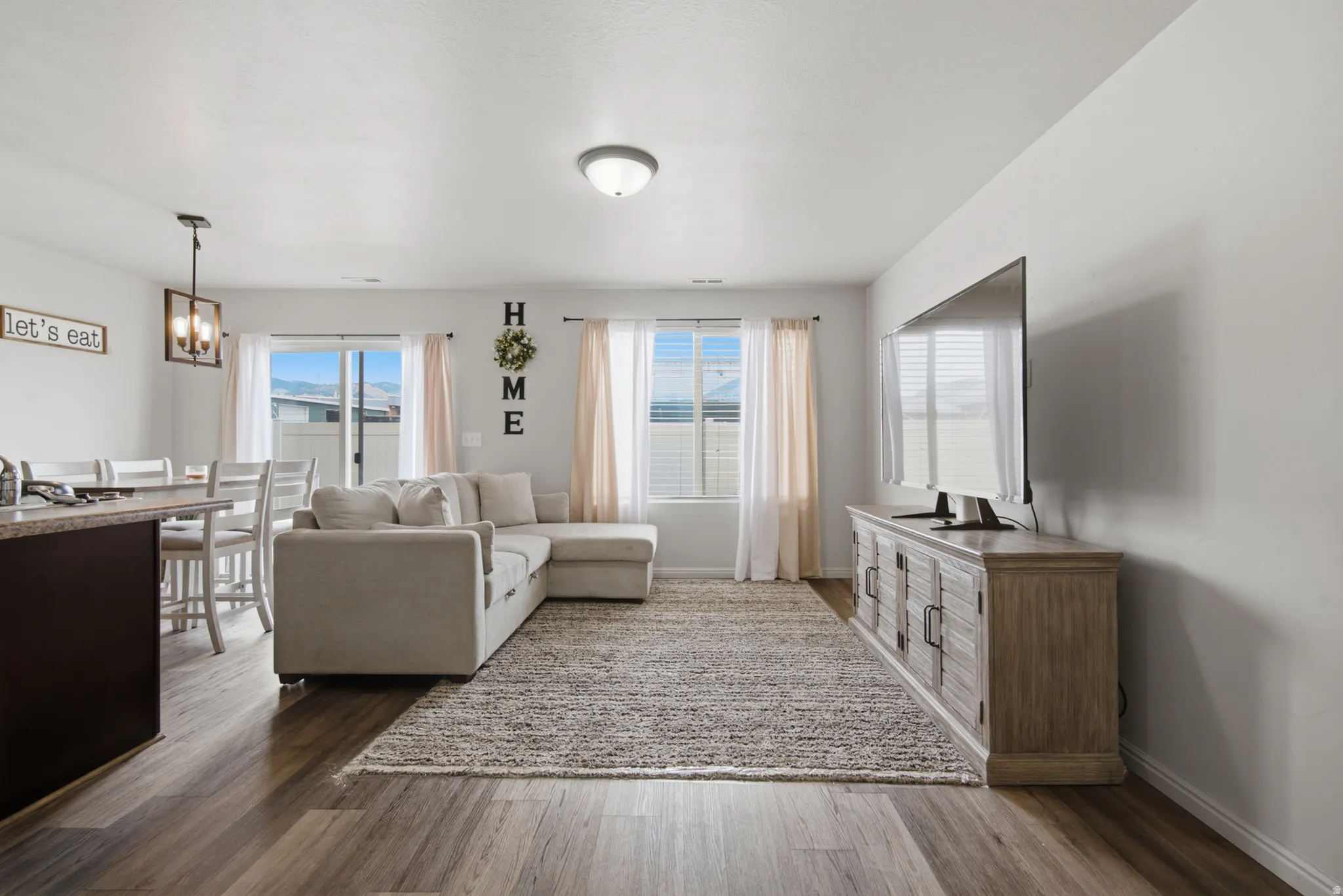 Open-concept living area featuring wood-finish flooring, recessed lighting, and large windows with blinds