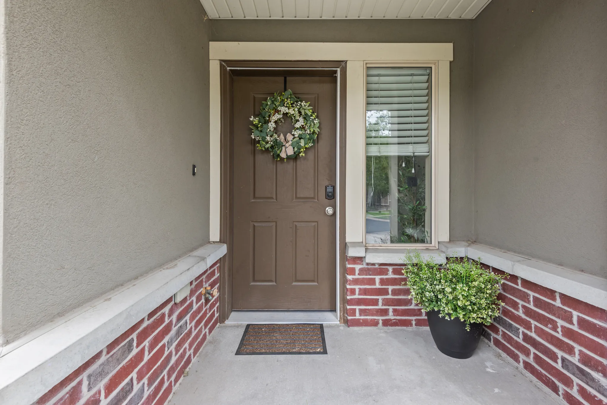 Stucco exterior with brick veneer detailing, concrete porch, and a paneled entry door with an adjacent window