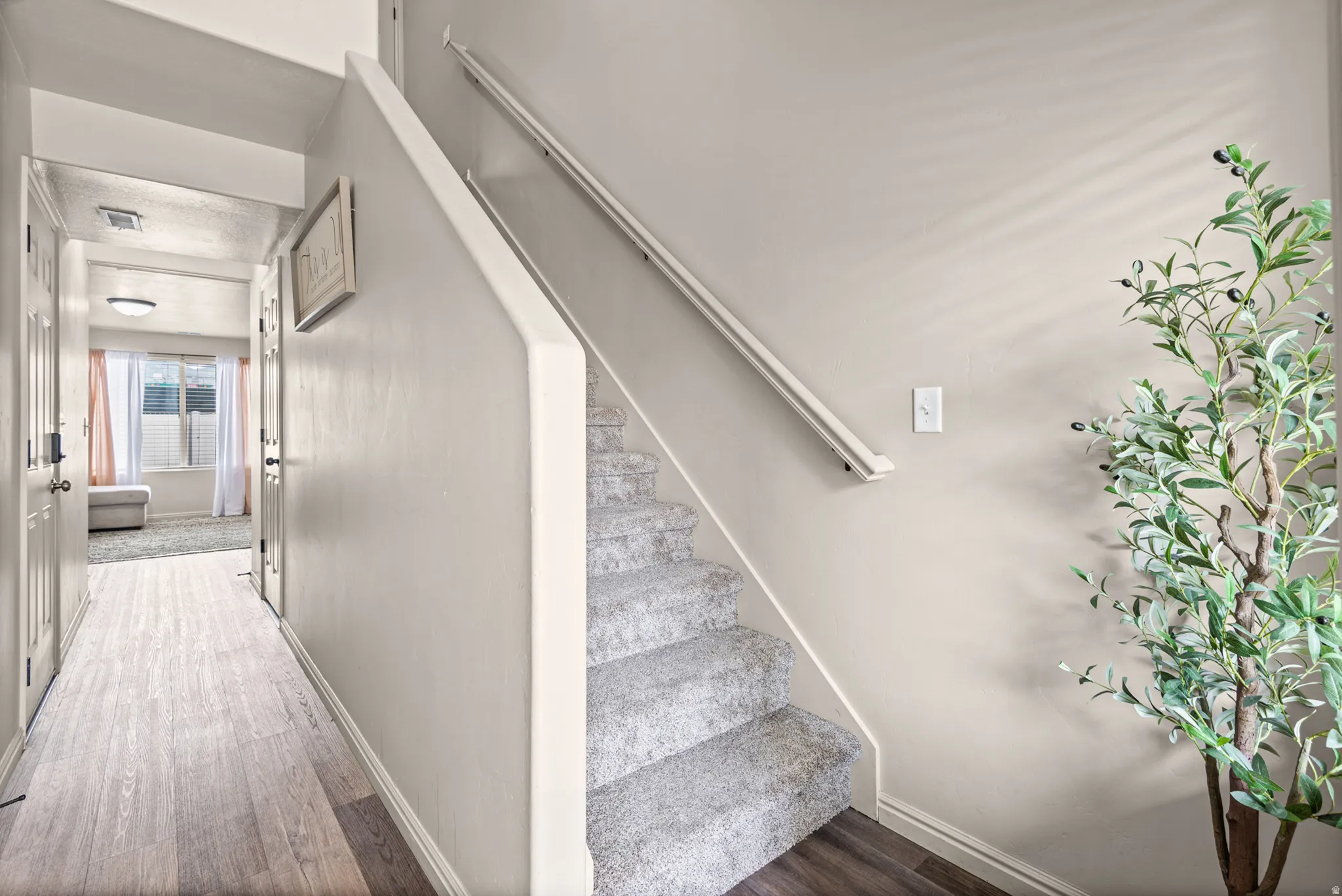 Carpeted staircase with white handrail, light wood-finish flooring in hallway, and neutral wall paint