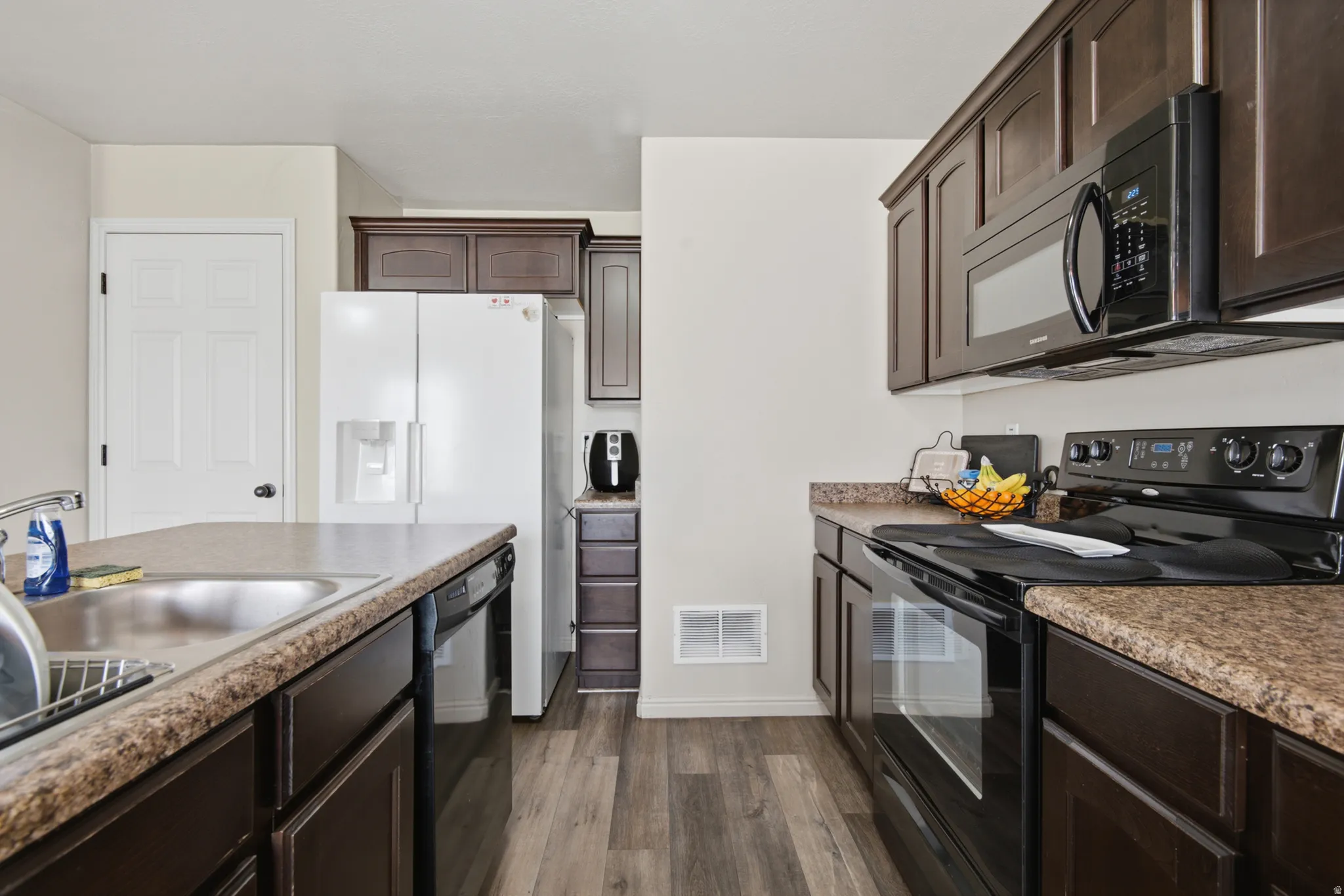 Kitchen featuring dark wood-finish cabinetry, wood-finish flooring, a stainless steel sink, and dark stone-look countertops