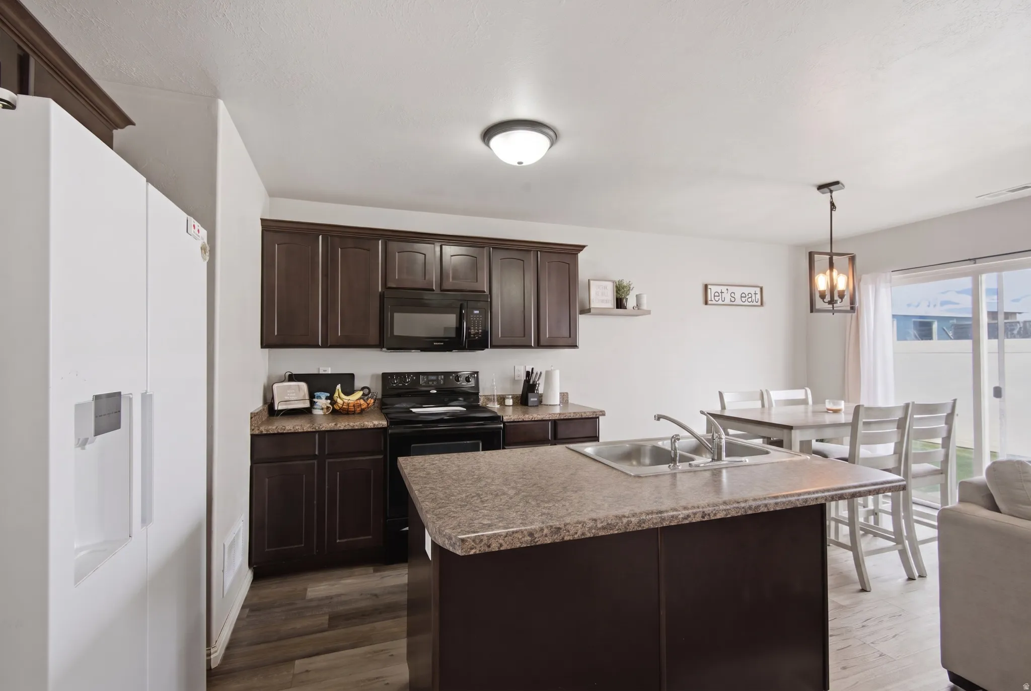 Kitchen featuring dark wood-finish cabinetry, black appliances, a central island with a double basin sink, and wood-finish flooring