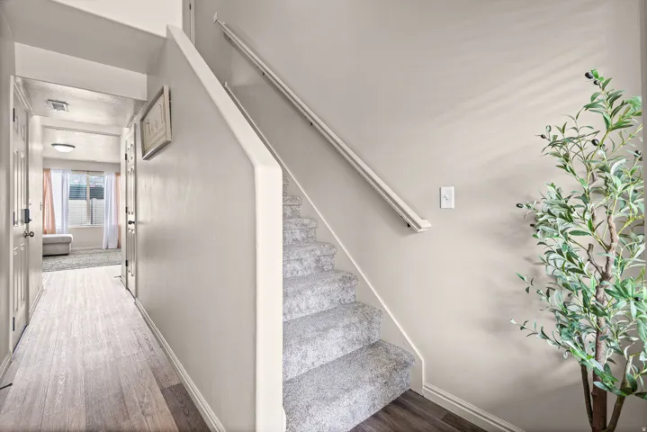Carpeted staircase with white handrail, light wood-finish flooring in hallway, and neutral wall paint