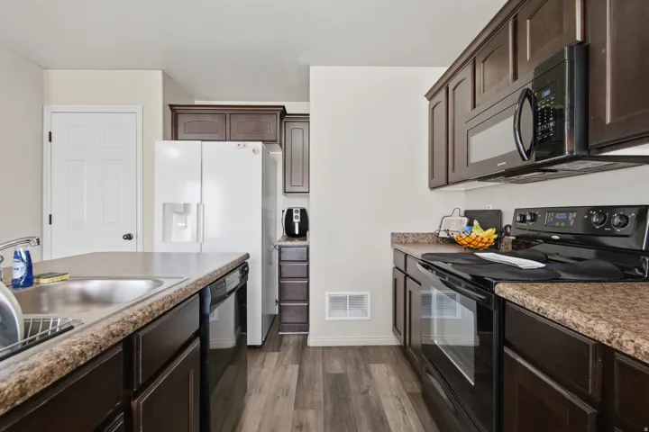 Kitchen featuring dark wood-finish cabinetry, wood-finish flooring, a stainless steel sink, and dark stone-look countertops