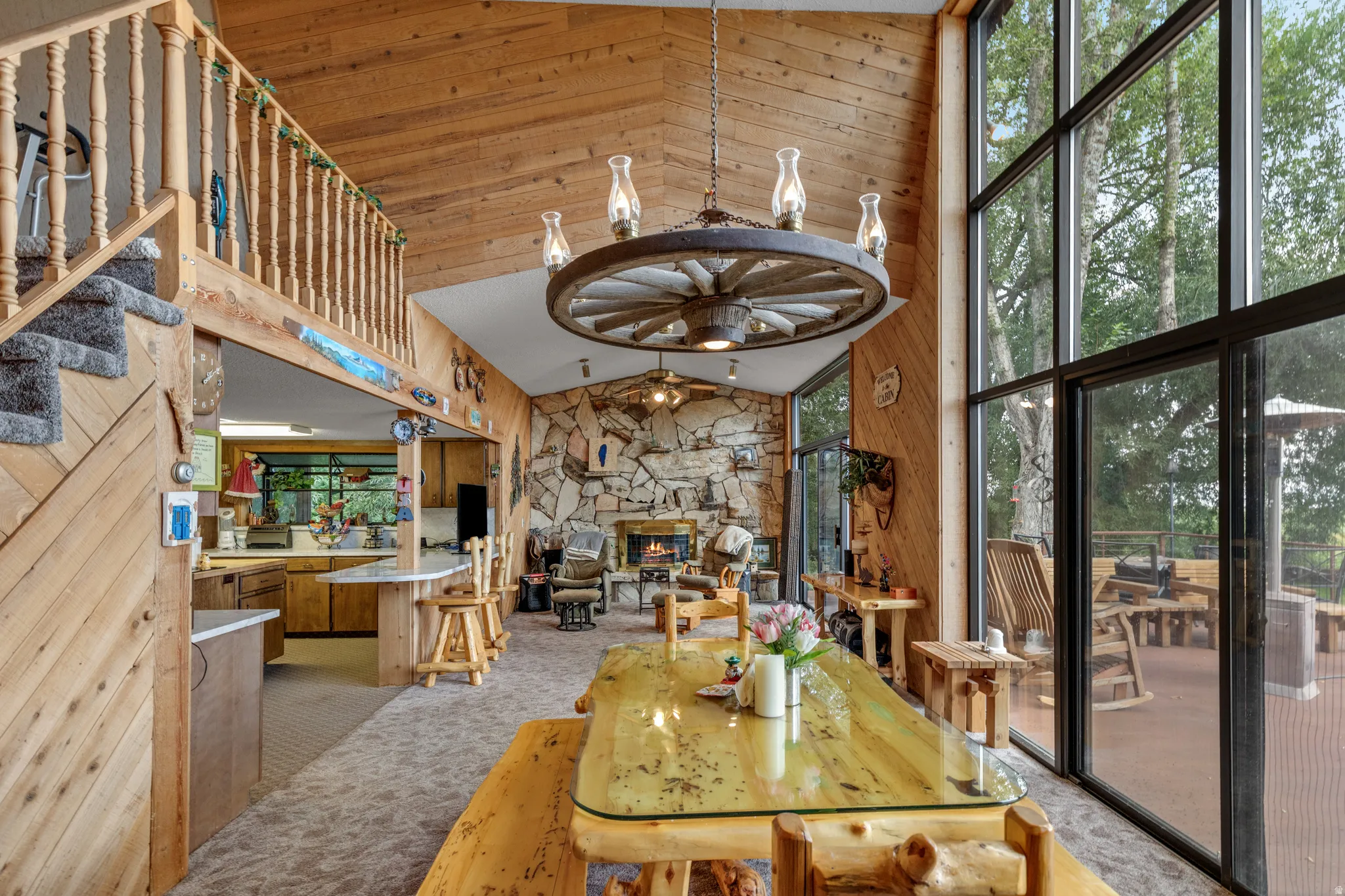 Vaulted wood-paneled ceiling, floor-to-ceiling window wall, stone fireplace, wood-finish flooring, and a kitchen island with seating