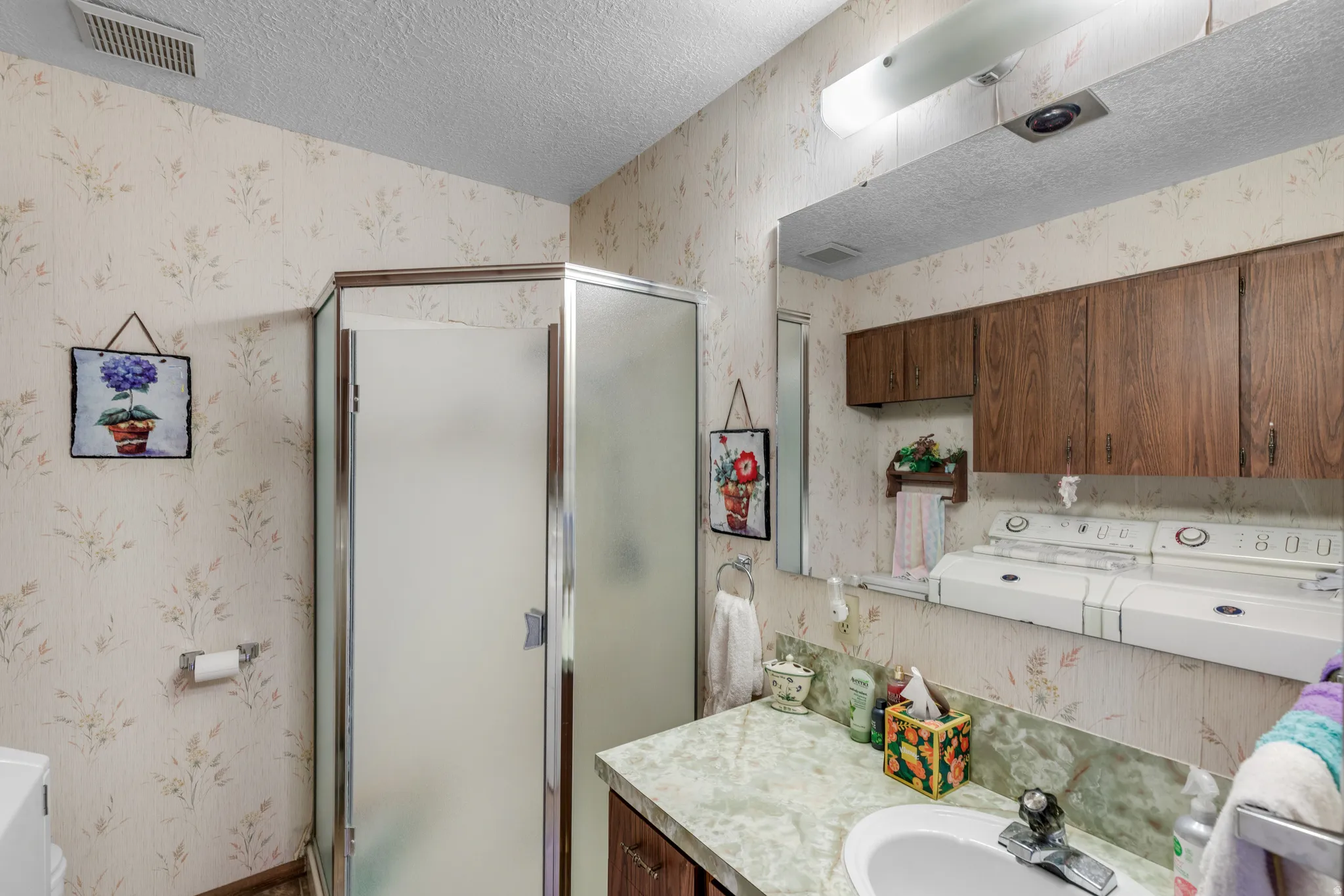 Enclosed corner shower with frosted glass, expansive vanity mirror, and wood-finish cabinetry