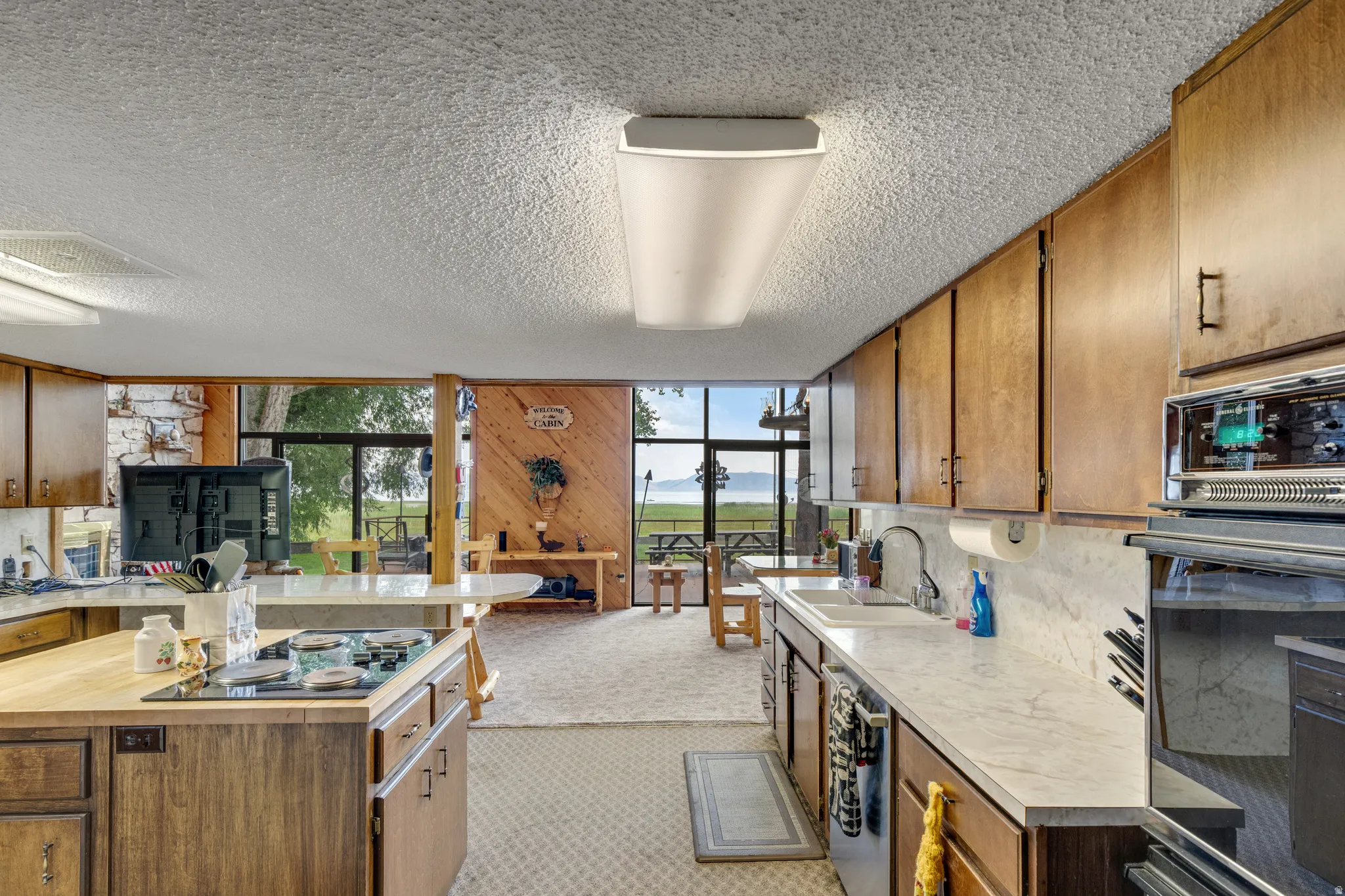 Open-concept kitchen with wood-finish cabinetry, built-in wall oven, and white countertops