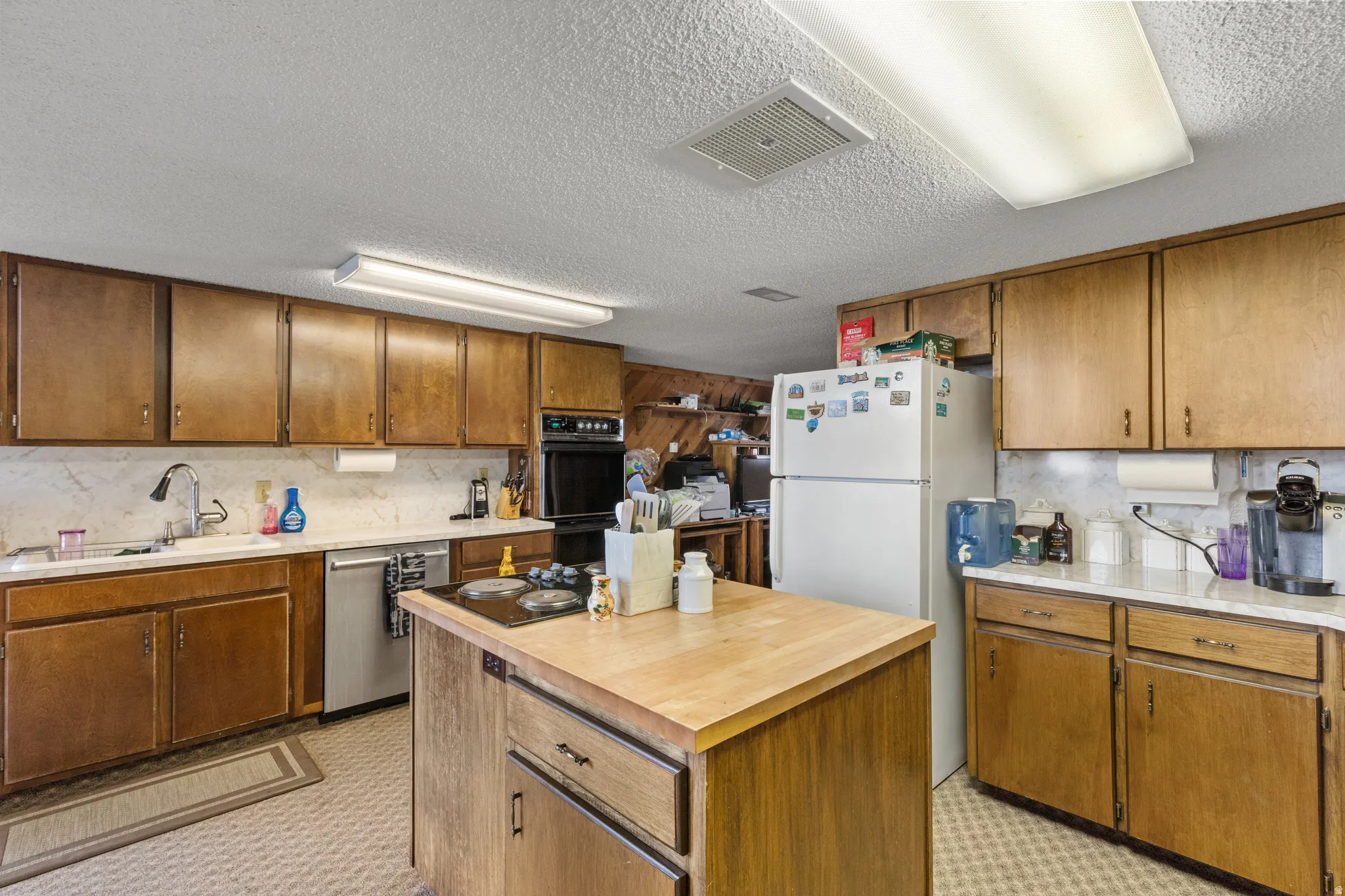 Kitchen featuring wood-finish cabinetry, a central island with a wood-finish countertop, a built-in oven, and white countertops