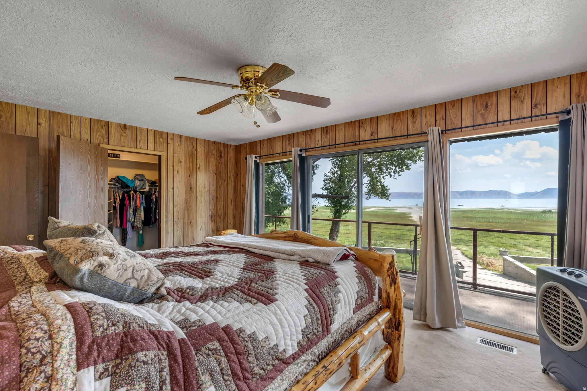 Master bedroom suite with wood-paneled walls, ceiling fan with brass fixtures, wood-finish flooring, and sliding glass doors opening to a private balcony