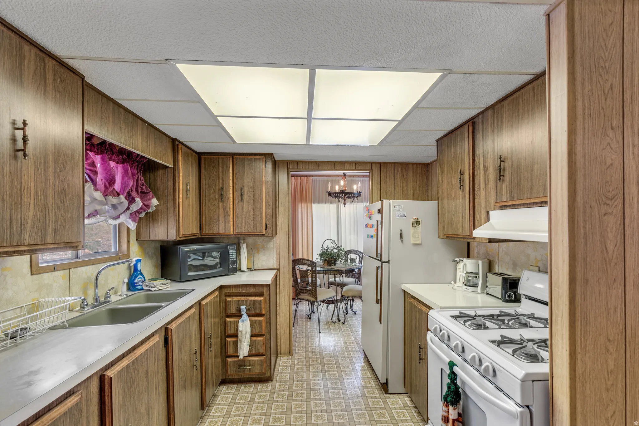 Kitchen featuring wood-panel walls, wood-finish cabinetry, and a dual basin stainless steel sink