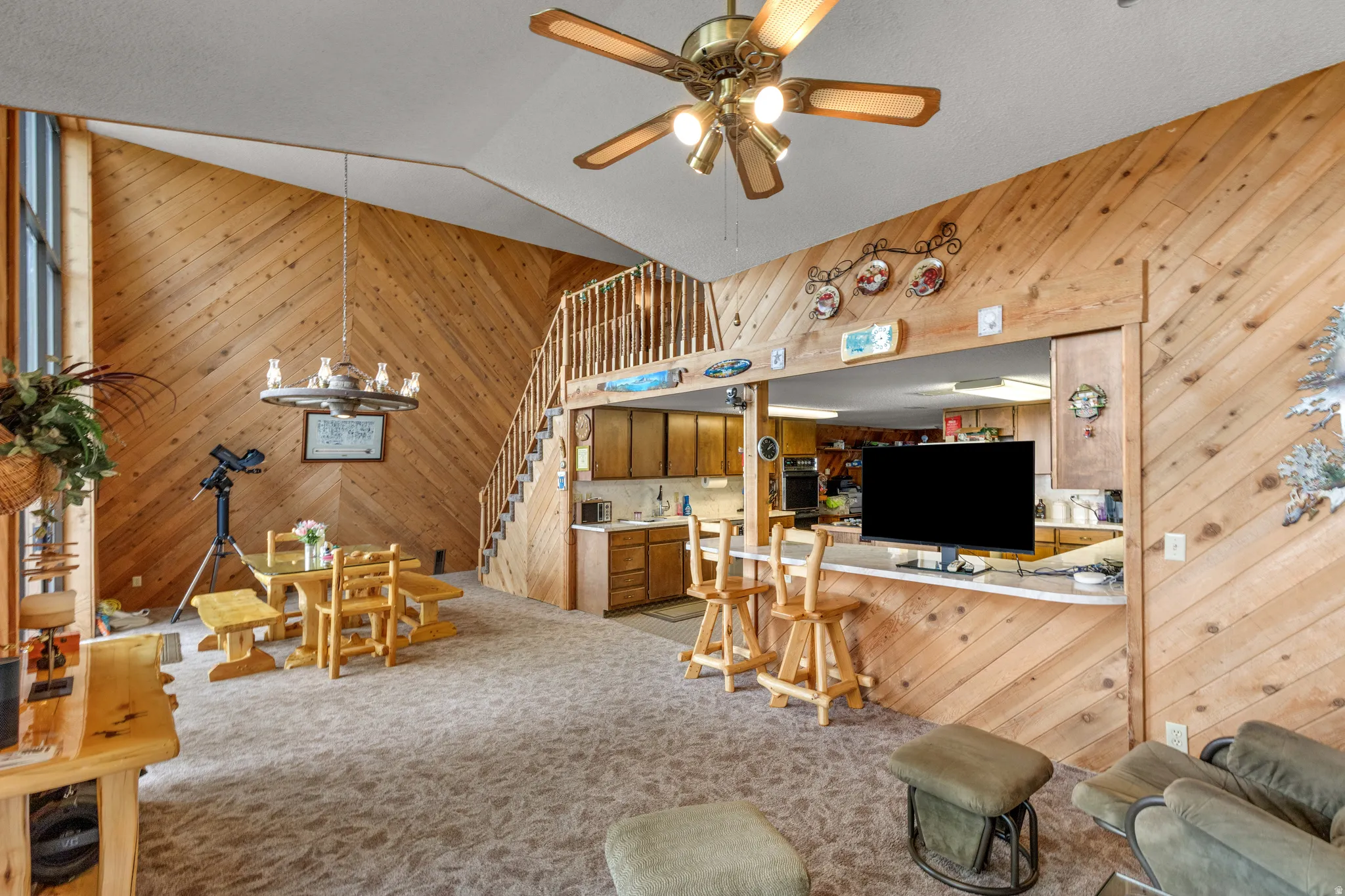 Vaulted ceiling with a ceiling fan, diagonal wood-paneled walls, built-in breakfast bar, and a wood staircase with a railing
