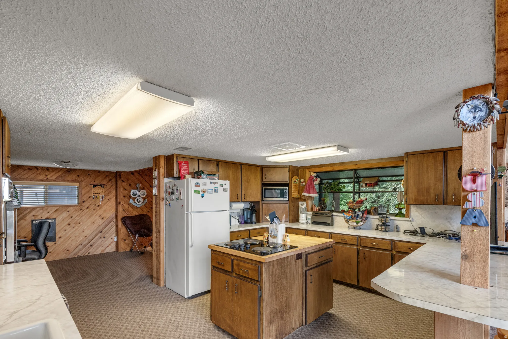 Kitchen featuring wood cabinetry, white countertops, built-in microwave, and a center island with a cooktop