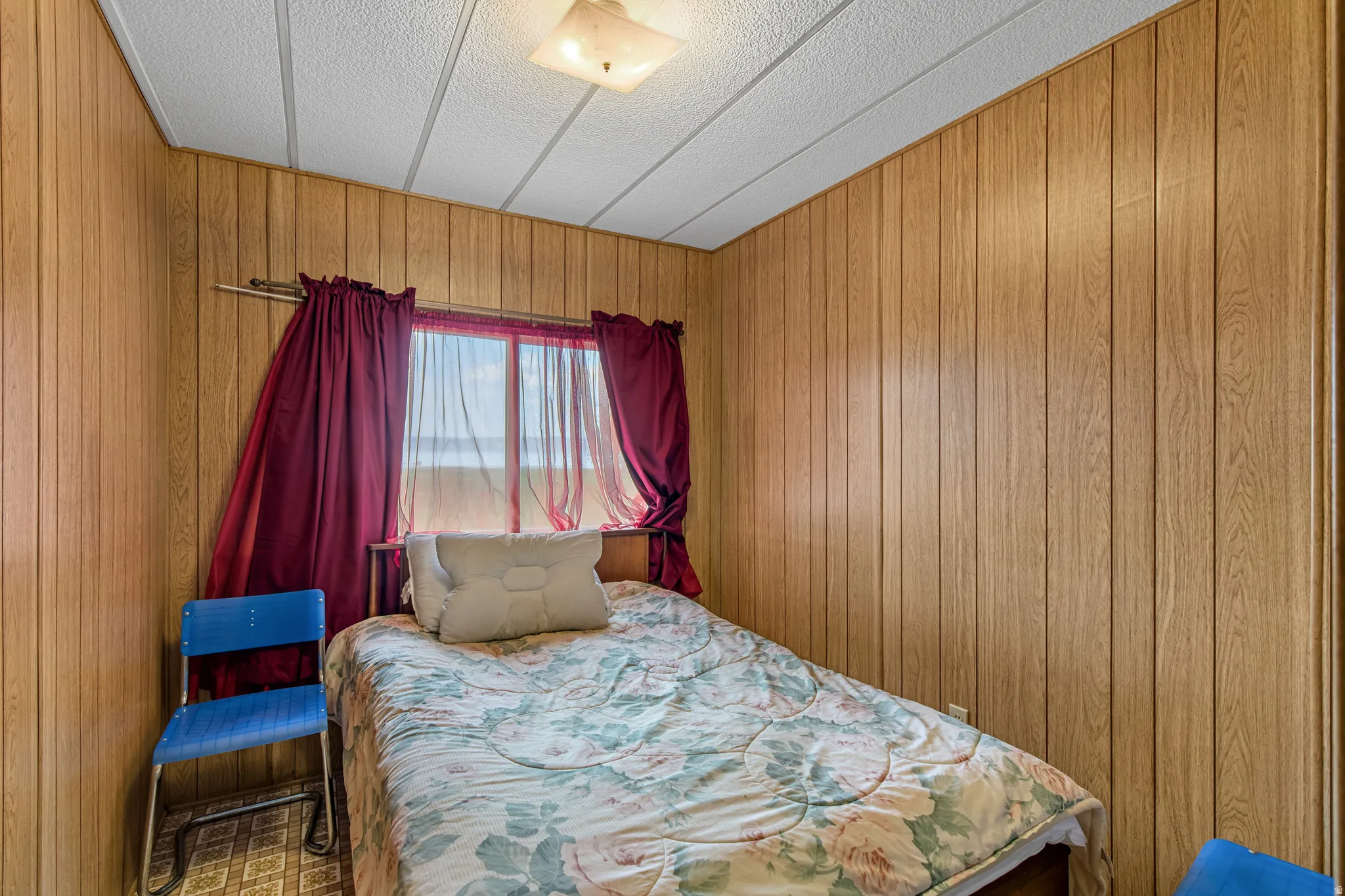 Wood-finish wall paneling, drop ceiling with flush-mount lighting, and a window with a sheer curtain