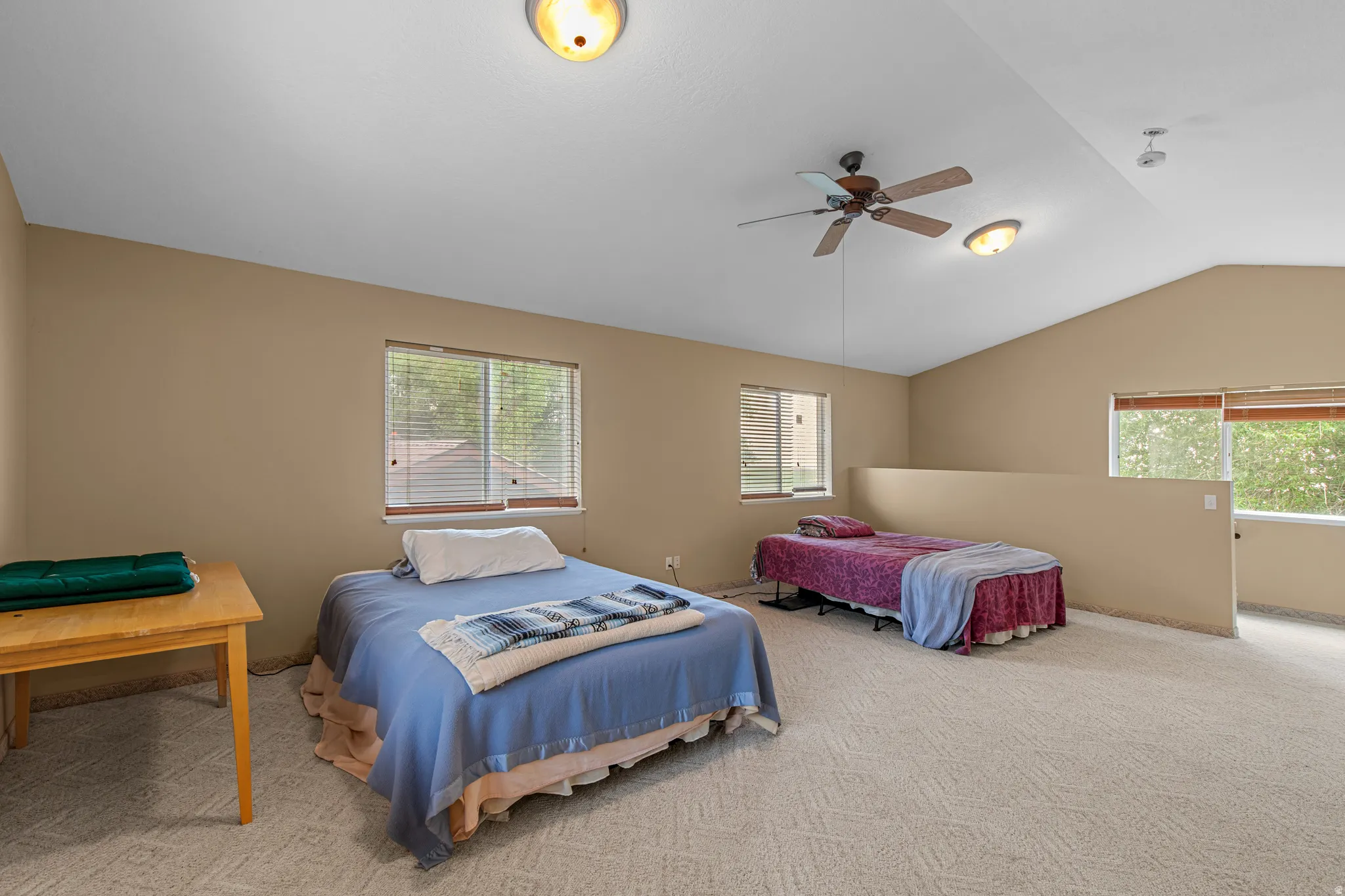 Vaulted ceiling with a ceiling fan, carpeted flooring, and multiple windows