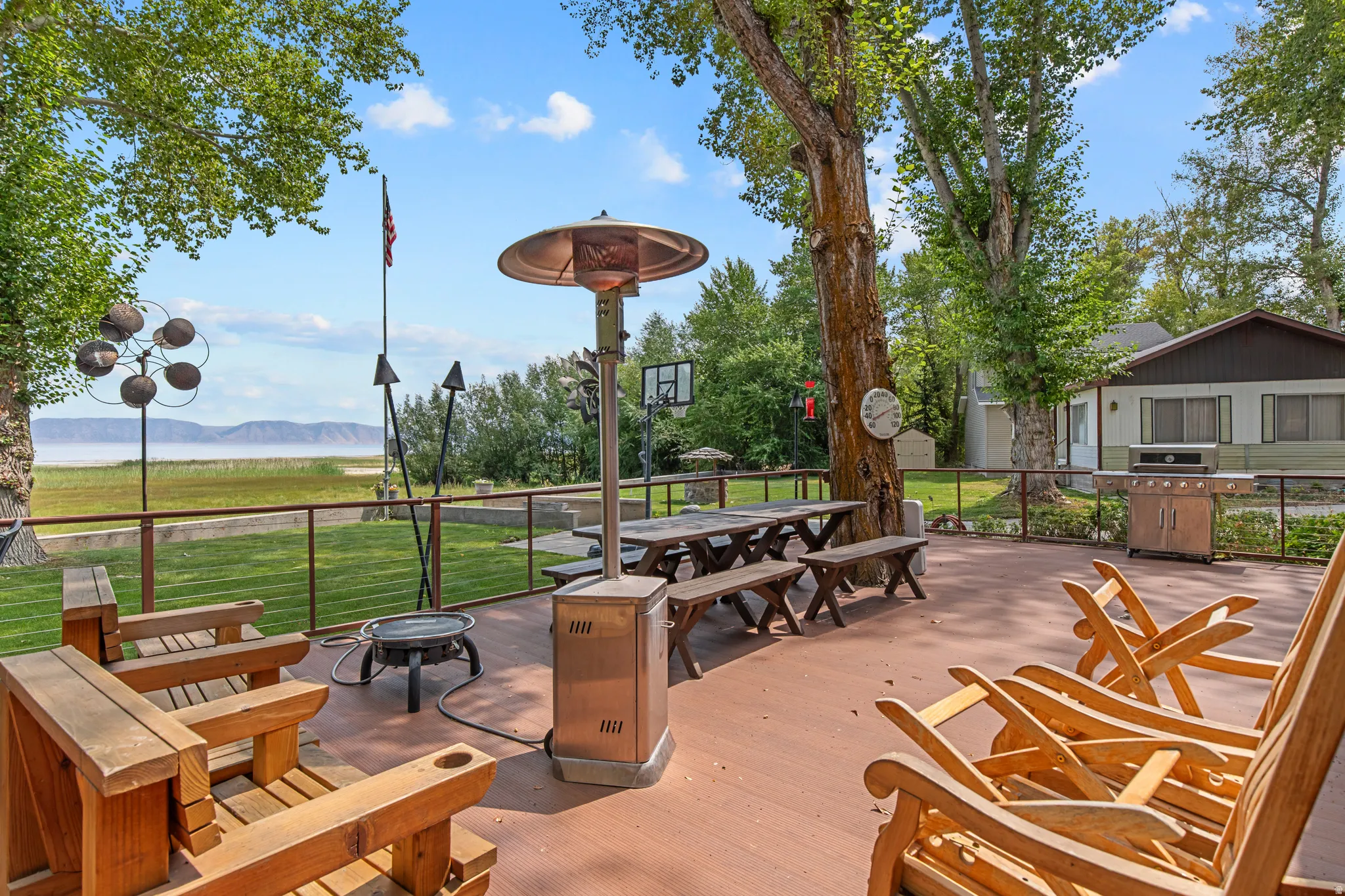 Expansive outdoor entertainment terrace featuring a wood-finish deck, mature shade trees, and waterfront vistas