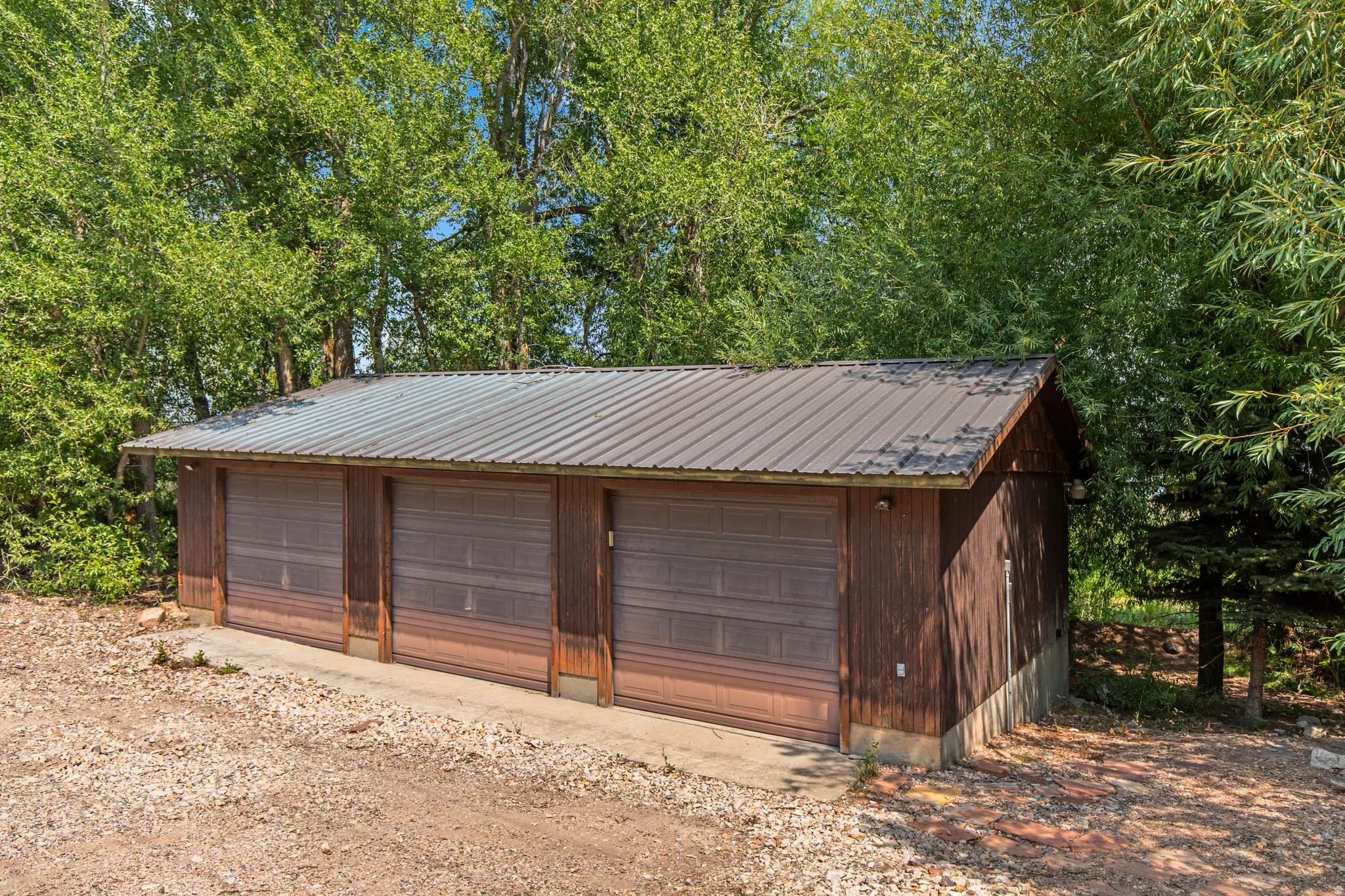 Three-bay garage with corrugated metal roofing, wood siding, and individual garage doors