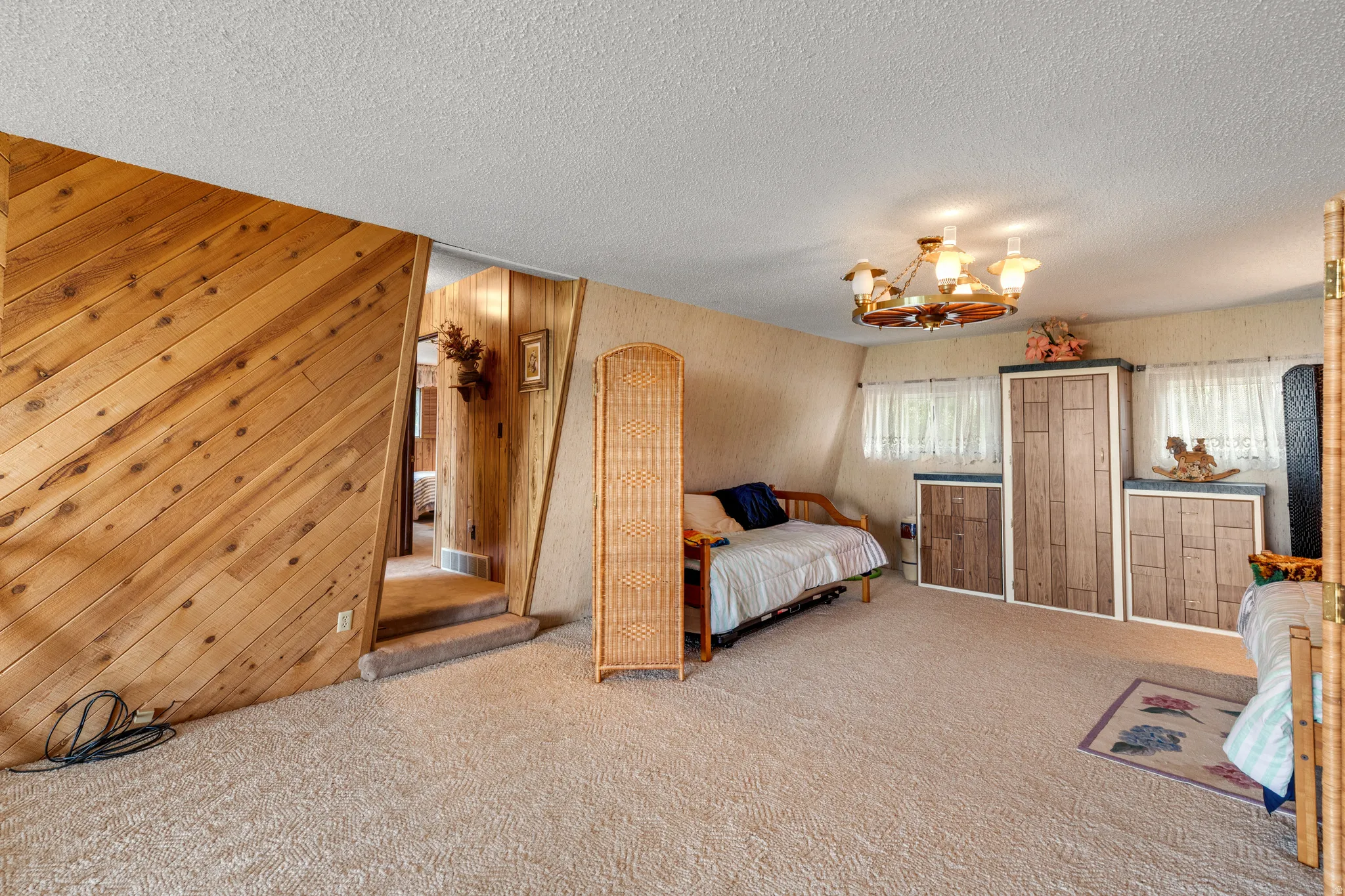 Angled wood paneling, sloped ceiling, built-in storage units, recessed windows, and a multi-arm chandelier