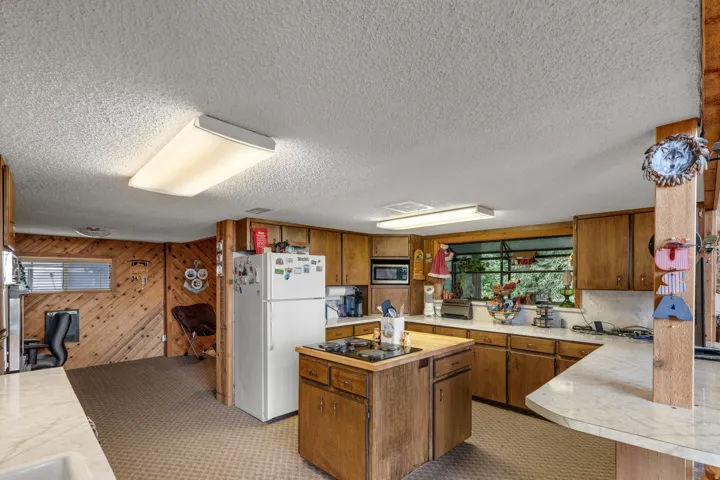 Kitchen featuring wood cabinetry, white countertops, built-in microwave, and a center island with a cooktop