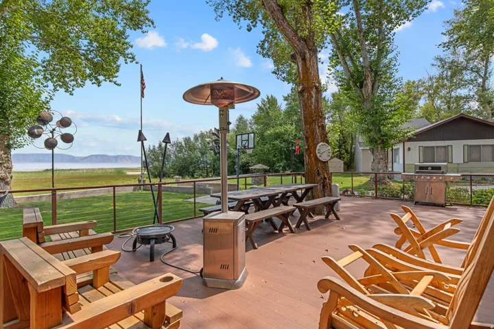 Expansive outdoor entertainment terrace featuring a wood-finish deck, mature shade trees, and waterfront vistas