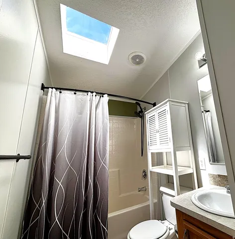 Skylight for natural illumination, recessed lighting, white wall-mounted storage cabinet, and a built-in bathtub with integrated shower