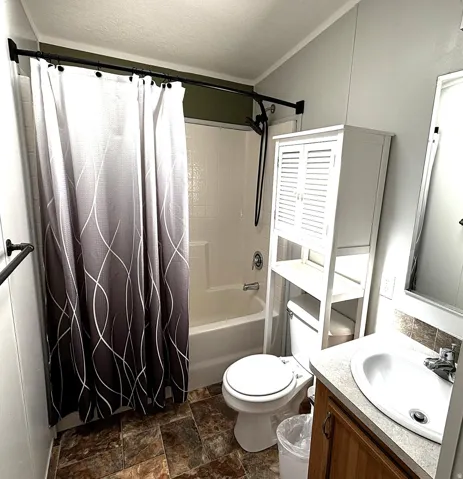 Bathtub with shower, white toilet, vanity with integrated sink, and wood-finish cabinetry