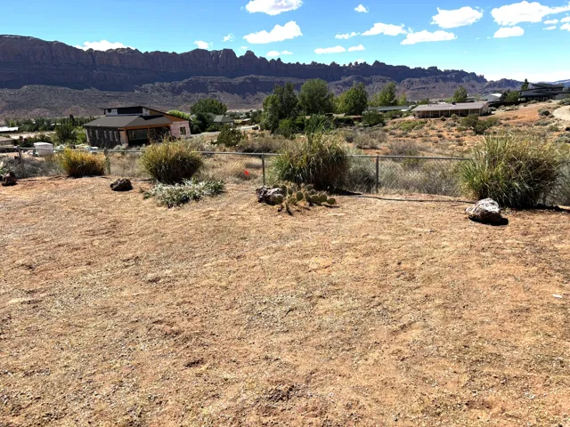 Expansive open lot with distant mountain backdrop, featuring scattered desert vegetation, chain-link fencing, and a clear sky