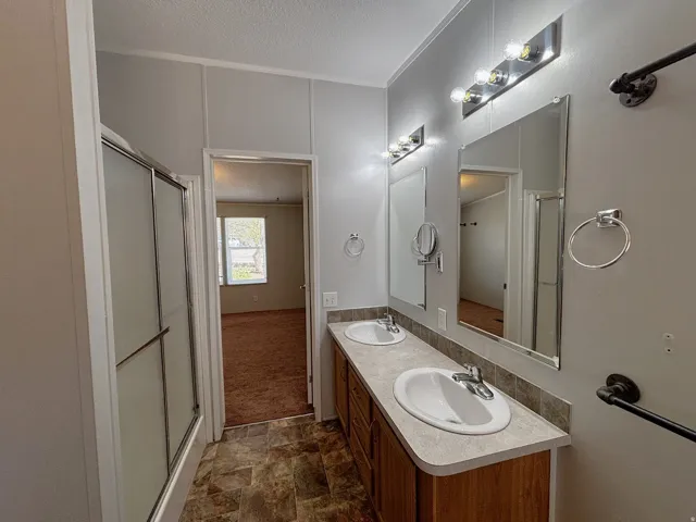 Primary suite bathroom. Dual vanity with integral sinks, tile-finish flooring, and a glass-enclosed shower