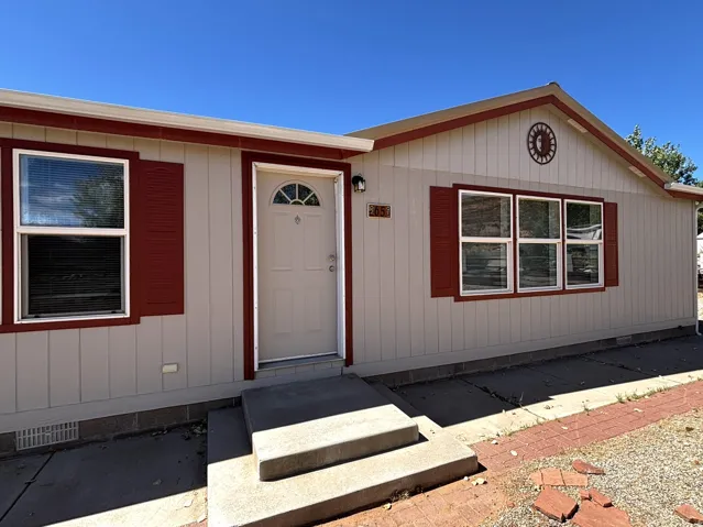 Single-story exterior with light-colored vertical siding, red trim, and red decorative shutters