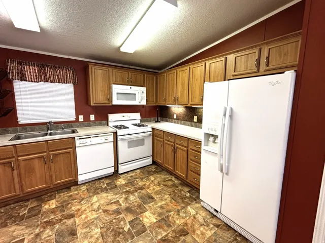Kitchen featuring wood-finish cabinetry, a double basin stainless steel sink, white appliances, and a tiled backsplash