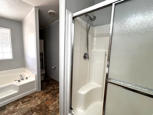 Ensuite bath with oversized tub,  shower  with integrated seating, chrome shower fixtures, and a sliding frosted glass shower door