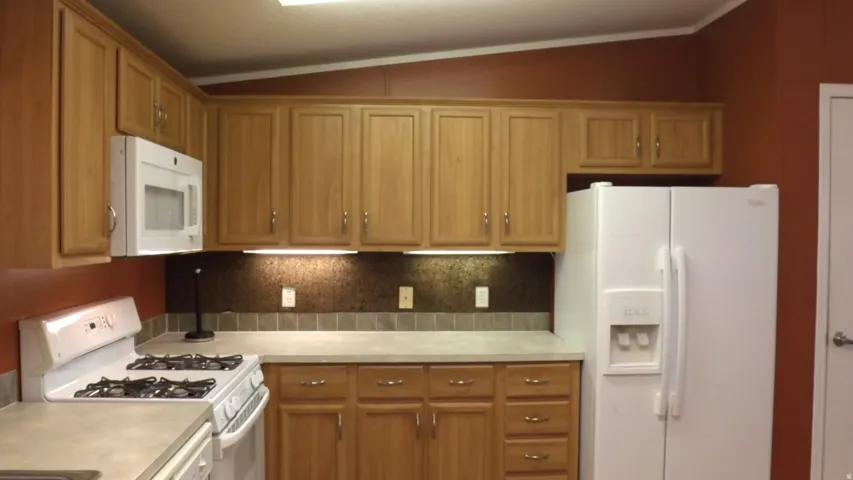 Kitchen featuring wood-finish cabinetry, built-in microwave, white refrigerator, and gas range