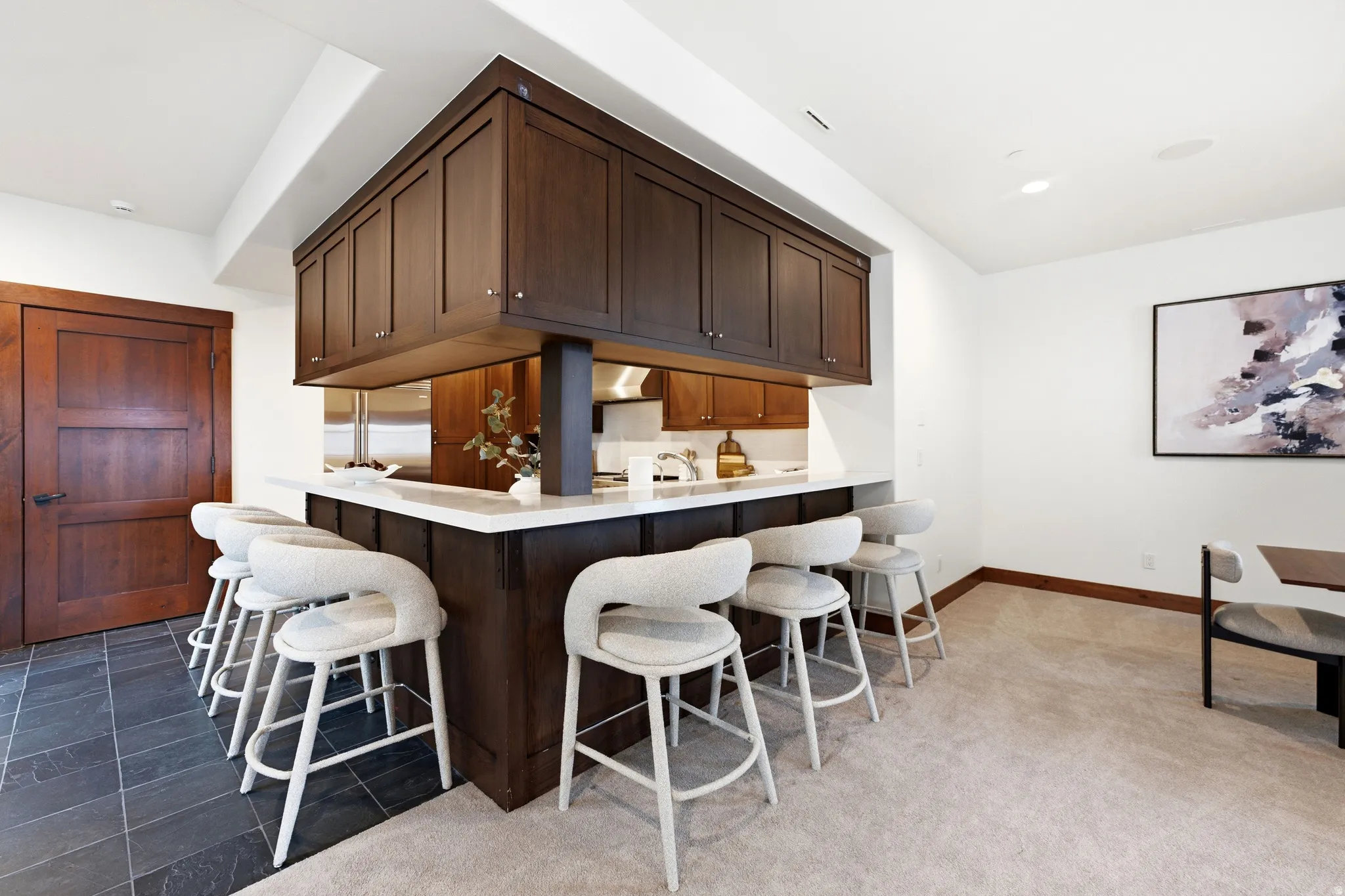 Sophisticated wet bar featuring a custom wood-finish cabinetry surround with integrated upper storage, white quartz countertop, and seating for six at coordinating bar stools