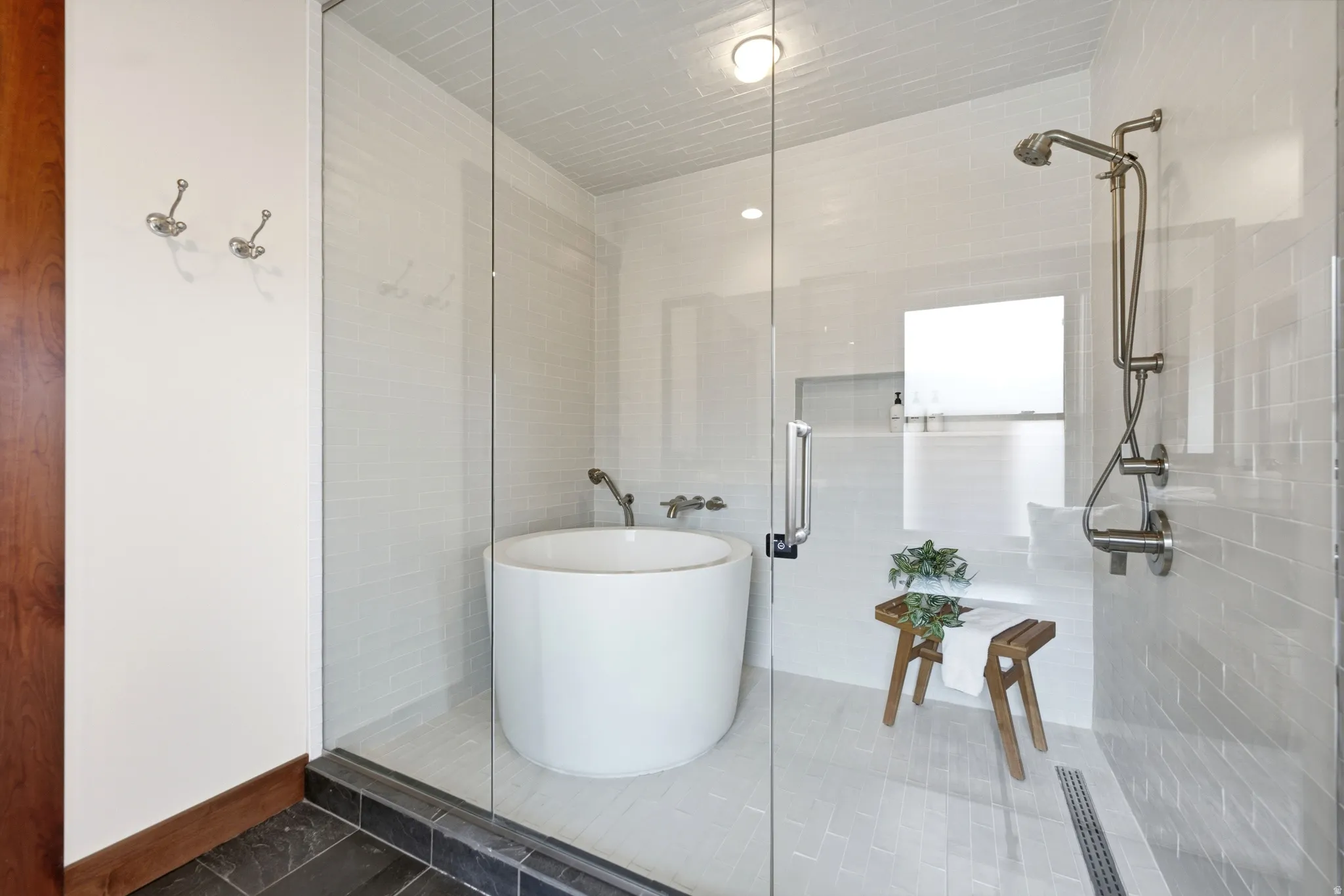 Enclosed shower with clear glass panels, a circular soaking tub, subway tile walls, a rain shower head, and a linear shower drain