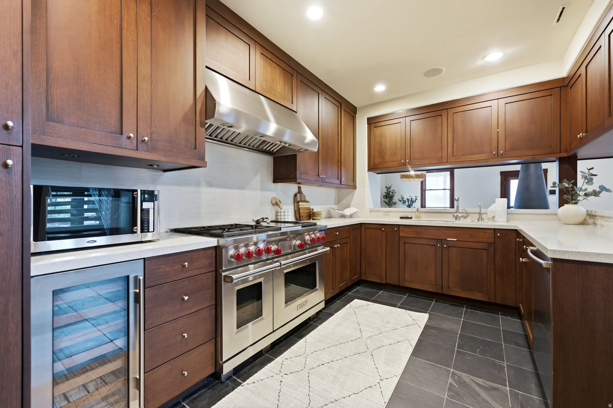 Hardwood cabinetry, stainless steel range with hood, stone countertops, integrated microwave, and beverage refrigerator