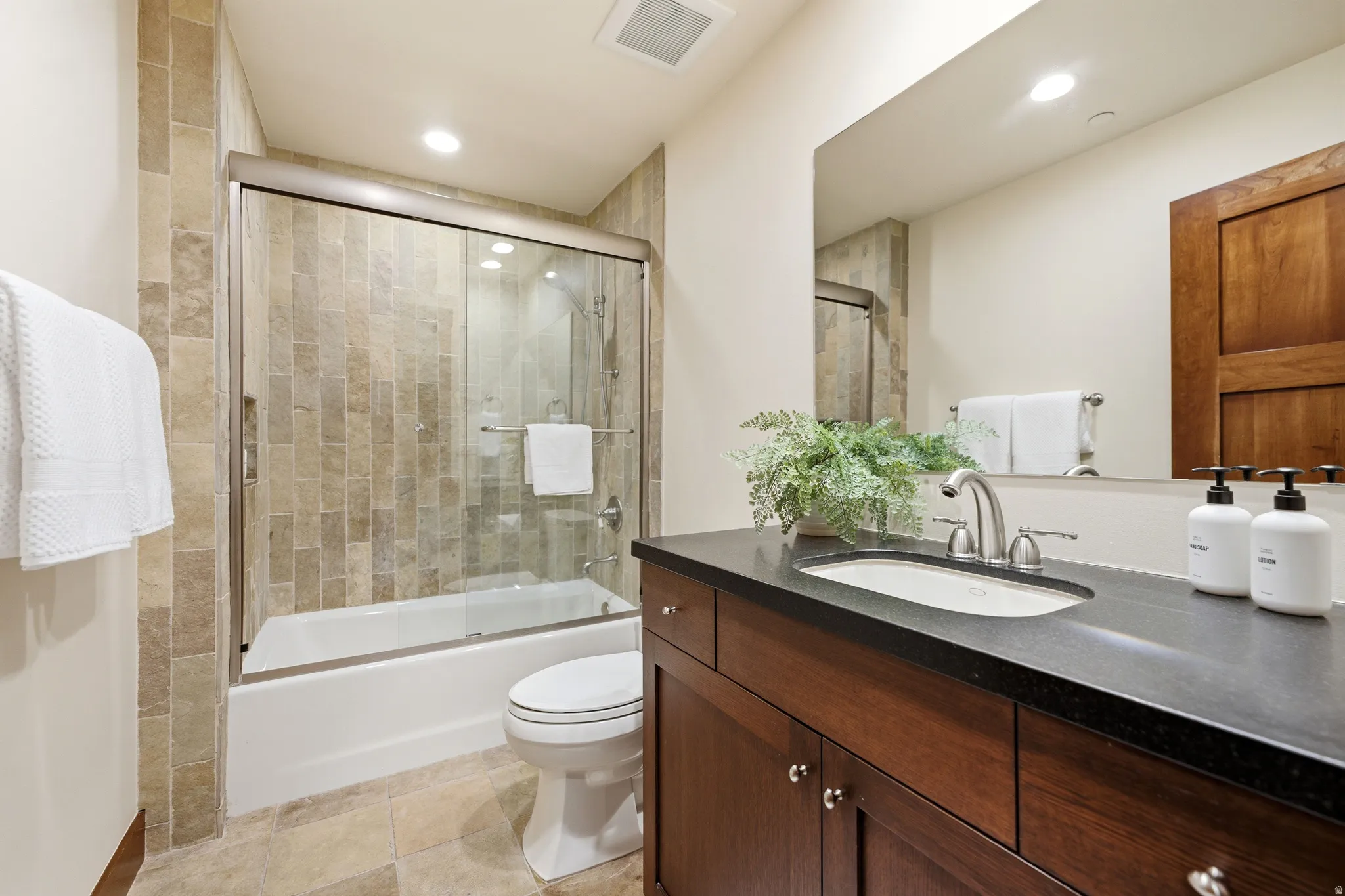 Bathroom featuring a wood-finish vanity with an undermount sink, dark stone countertop, and brushed nickel fixtures