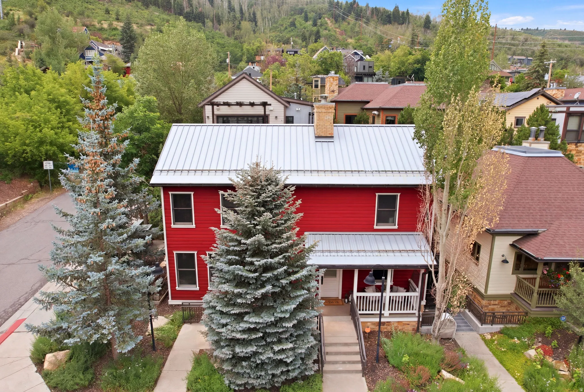 Red exterior with a white porch, metal roof, and brick chimney