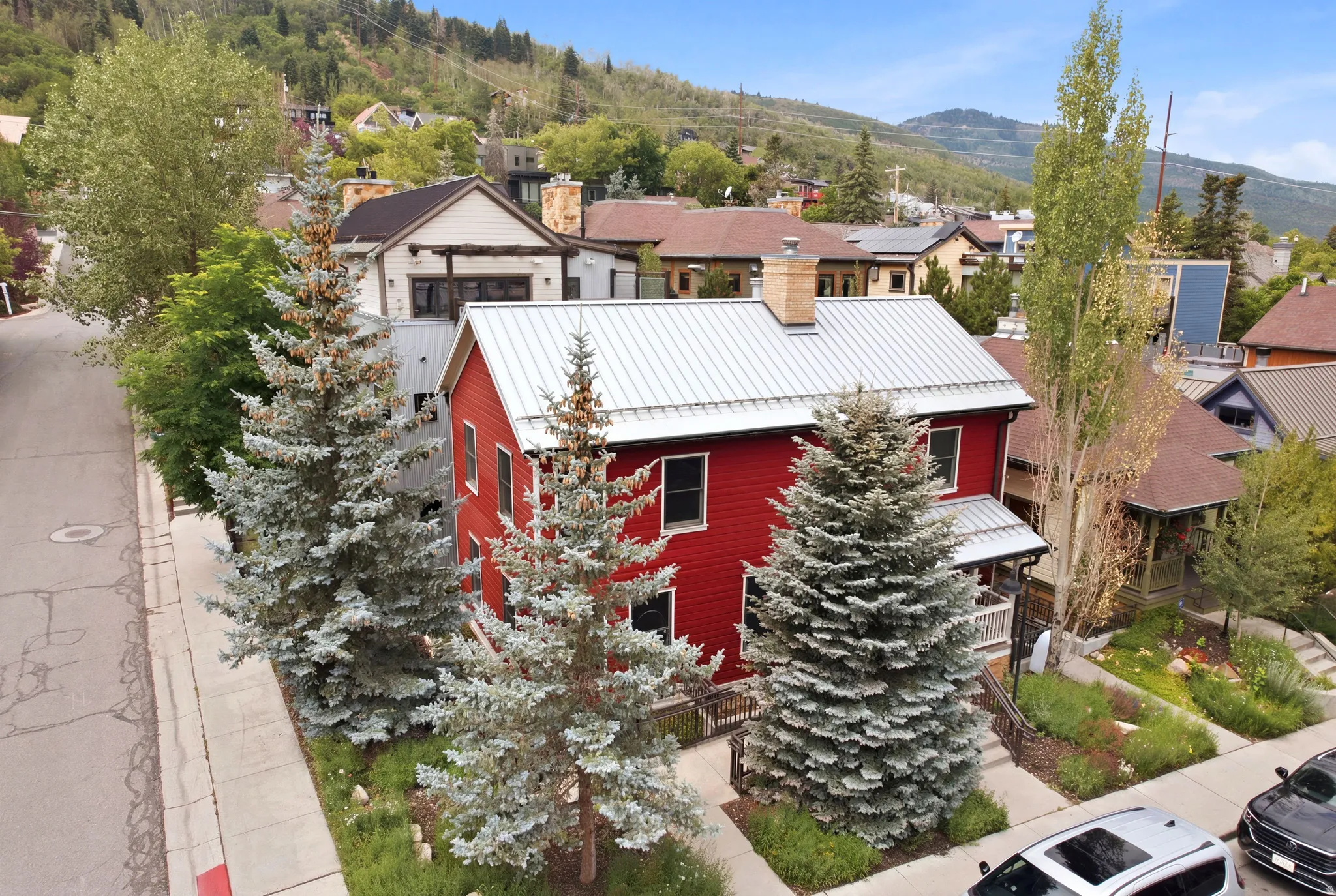 Red-sided exterior with a metal roof, front porch, and mature evergreen trees